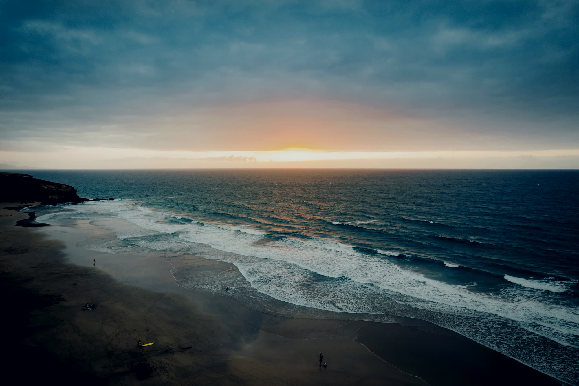 A dark coastline at dusk with surf running onto the sand.