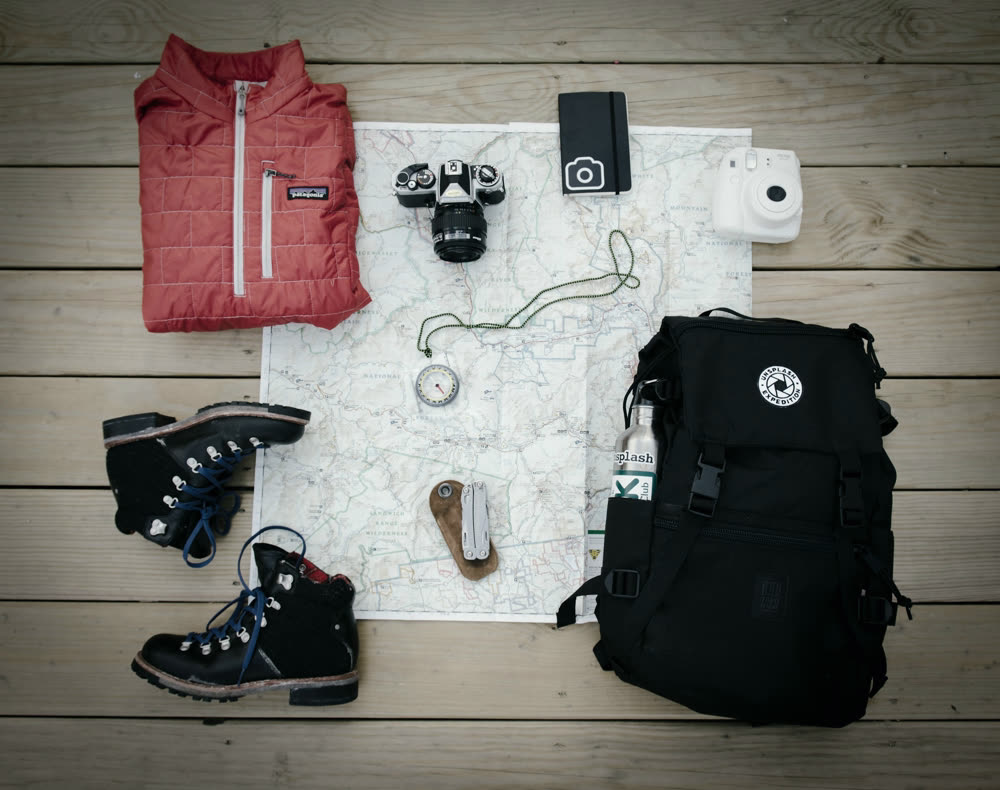 Expedition equipment laid out in a grid: boots, pack, camera, map.