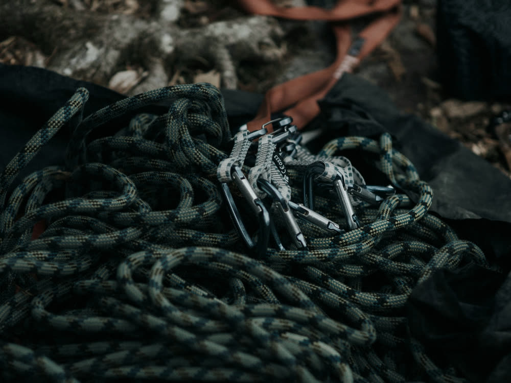 A coiled climbing rope with carabiners in low light.